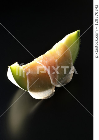 Raw ham and melon photographed against a black background 129570842
