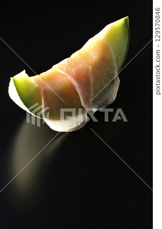 Raw ham and melon photographed against a black background 129570846