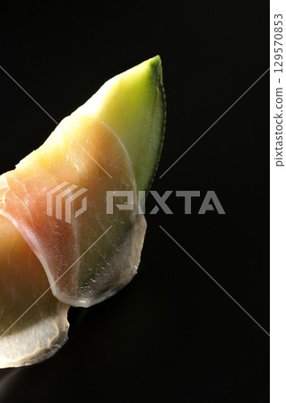 Raw ham and melon photographed against a black background 129570853