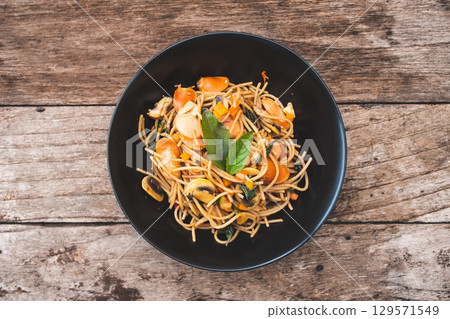 Homemade Spicy Sausage Spaghetti with basil on the black plate on the wooden table, Thai style Homemade Spicy Sausage Spaghetti with basil on the black plate on the wooden table, Thai style 129571549