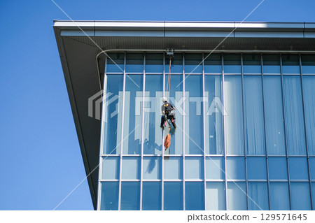 Worker cleaning glass building facade 129571645
