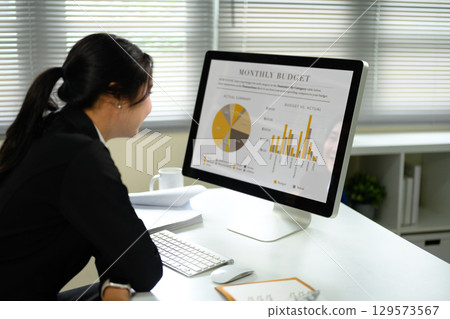 Female office worker reviewing a monthly budget report with pie and bar charts on a desktop screen Female office worker reviewing a monthly budget report with pie and bar charts on a desktop screen 129573567