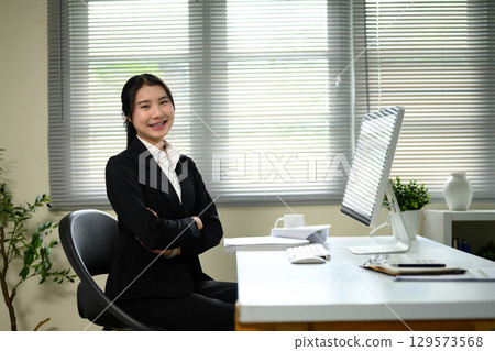 Young businesswoman smiling confidently with arms crossed in a modern office Young businesswoman smiling confidently with arms crossed in a modern office 129573568