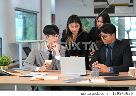 Confident professionals sharing ideas and working on laptops during a productive team discussion 129573639