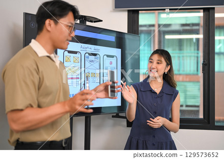 Creative team members discussing user interface layouts, during a mobile app design presentation 129573652