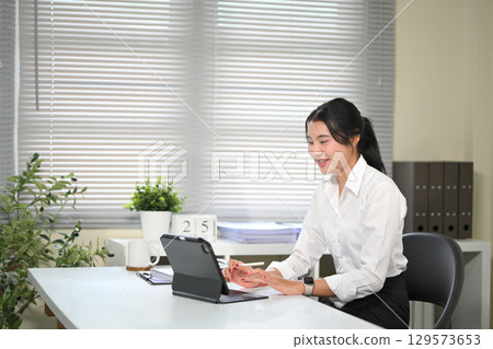 Young woman smiling during a virtual meeting using digital tablet at a bright home office 129573653