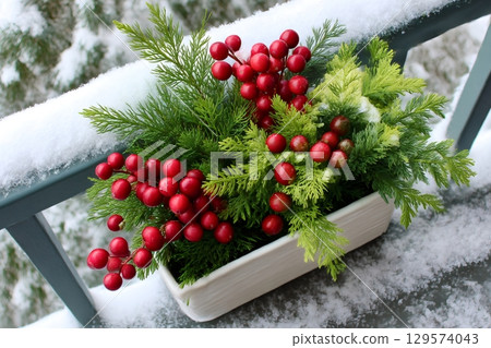 Christmas decoration with red berries and green branches resting on snowy railing 129574043