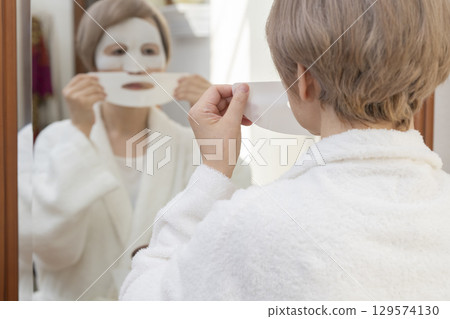 Senior woman taking care of her skin with a face mask in front of the mirror Senior woman taking care of her skin with a face mask in front of the mirror 129574130