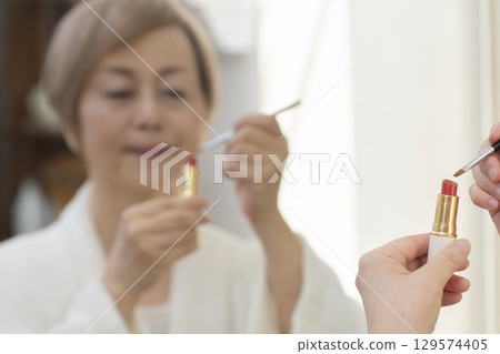 Senior woman putting on makeup in front of the mirror 129574405