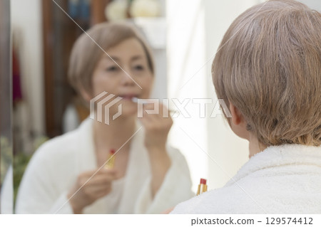 Senior woman putting on makeup in front of the mirror Senior woman putting on makeup in front of the mirror 129574412