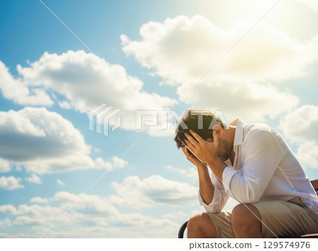 Man hides face in hands sitting outdoors in sweltering heatwave, sun shining hard above with little shade or relief Man hides face in hands sitting outdoors in sweltering heatwave, sun shining hard above with little shade or relief 129574976