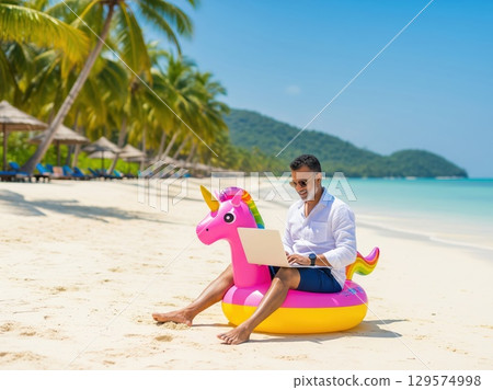 Man lounging on unicorn float with laptop on sunny beach, combining business and pleasure for ideal remote working getaway 129574998