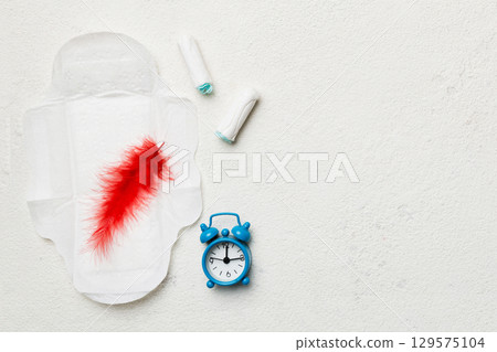 Ringing alarm clock with sanitary female tampons and menstrual sanitary pads. Medical concept of woman critical days and menstruation. Female daily hygiene. Copy space 129575104