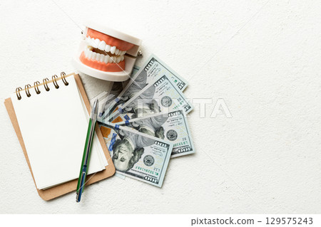Flat lay composition with educational dental typodont model and money with notebook on colored table, top view. Expensive treatment Flat lay composition with educational dental typodont model and money with notebook on colored table, top view. Expensive treatment 129575243