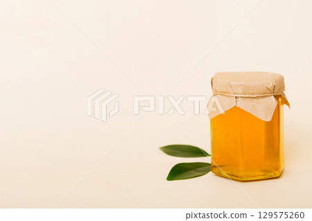 Honey in jar with leaves and honey dipper on colored background top view with copy text 129575260