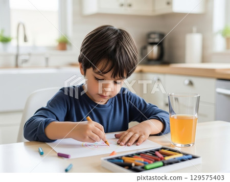 Focused child drawing intently at a sunlit table with crayons and juice nearby 129575403