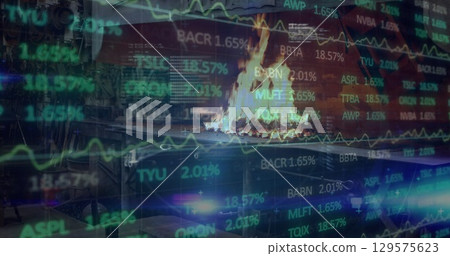 Burning metal fire pit casting flickering flames in courtyard, with stock ticker overlays 129575623