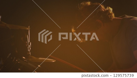 Image of caucasian male drummer playing drum kit, under orange coloured lights Image of caucasian male drummer playing drum kit, under orange coloured lights 129575739