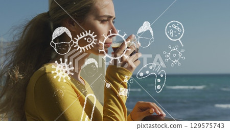 Image of pandemic icons over caucasian woman drinking coffee by sea 129575743