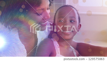 Image of light spots and trails over african american woman and her daughter cooking together 129575863