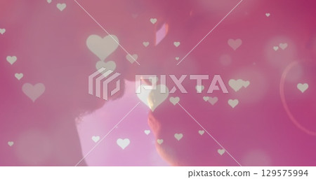 Image of glowing spots and hearts over diverse couple embracing 129575994