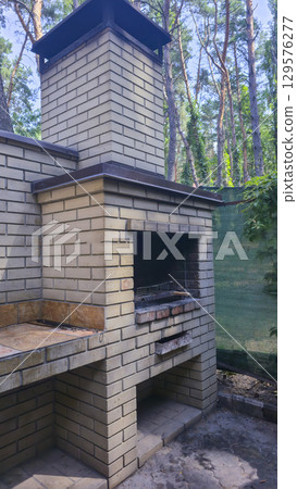 A tall brick oven in a gazebo in nature for cooking food on fire and skewers. 129576277