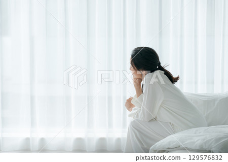 A woman in pajamas waking up in the morning and sitting on her bed A woman in pajamas waking up in the morning and sitting on her bed 129576832