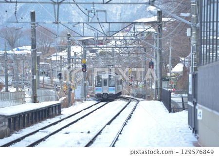 On January 2nd, at Obasute Station on the JR Shinonoi Line, where snow still remains, an E127 series local train tackles the switchback slope. 129576849