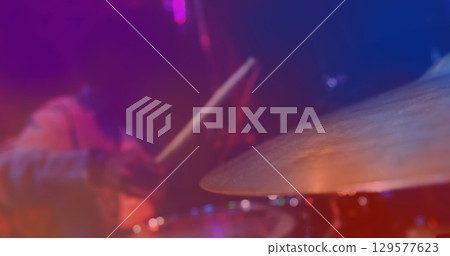 Image of red and blue light swirls over african american male drummer playing kit in slow motion 129577623