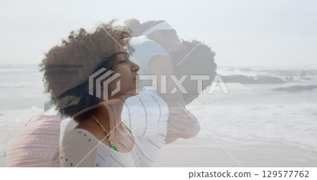 Image of african american parents and daughter playing on beach over woman meditating on beach Image of african american parents and daughter playing on beach over woman meditating on beach 129577762