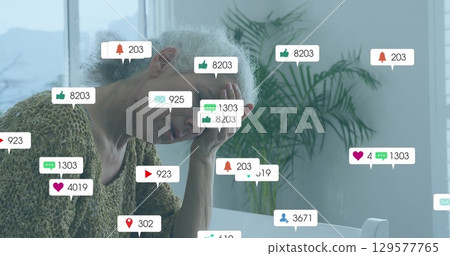 Propping head senior woman in sweater experiencing notification overload at home desk, with icons Propping head senior woman in sweater experiencing notification overload at home desk, with icons 129577765