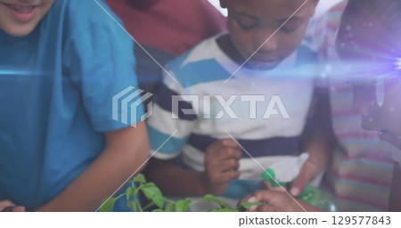 Image of light trails over diverse schoolchildren holding plants 129577843
