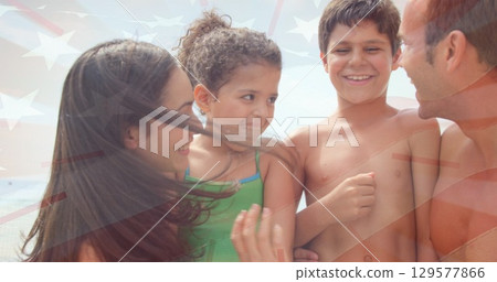 Standing family group wearing swimwear at sandy shoreline, with translucent national flag overlay 129577866