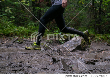 Legs athlete running mud and rocks during forest marathon 129579013