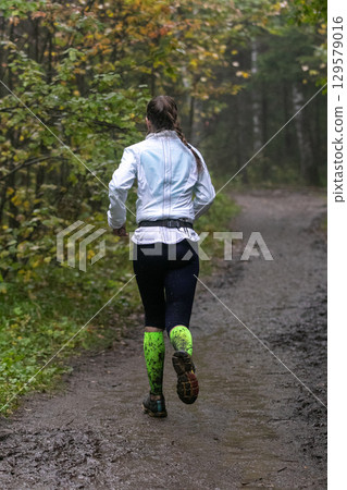 Female athlete running muddy forest trail during marathon in heavy rain 129579016