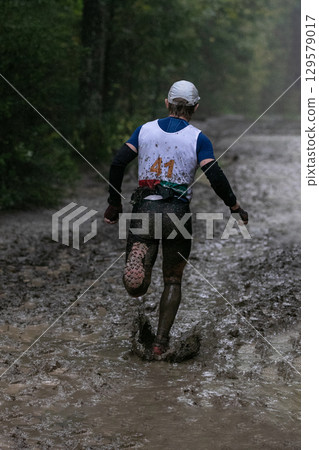 Athlete running muddy forest trail during marathon in heavy rain Athlete running muddy forest trail during marathon in heavy rain 129579017