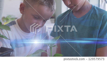 Image of light trails over diverse schoolchildren holding plant 129579573