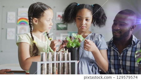 Image of light trails over diverse schoolchildren and teacher holding plants 129579574