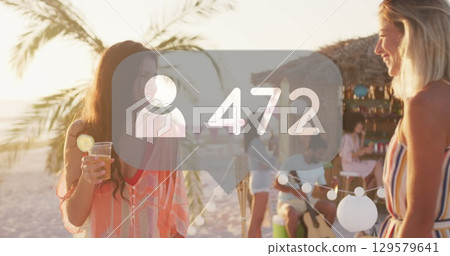 Image of profile icons with increasing numbers over two diverse female friends talking at beach 129579641