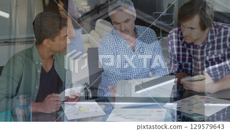 Three colleagues reviewing design sketches in office meeting room, with laptop, tablets, smartphone 129579643