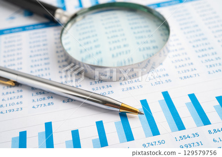 Magnifying glass on spreadsheet and graph paper. Magnifying glass on spreadsheet and graph paper. 129579756