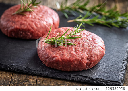 Raw burger beef patties on cutting board on wooden table. Raw burger beef patties on cutting board on wooden table. 129580058