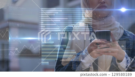 Image of flared lights with graphs over midsection of woman in scarf using smartphone 129580189