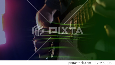 Image of green light trails over slow motion hand of musician playing electric guitar Image of green light trails over slow motion hand of musician playing electric guitar 129580270