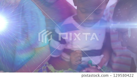 Image of light trails over diverse schoolchildren holding plants 129580422