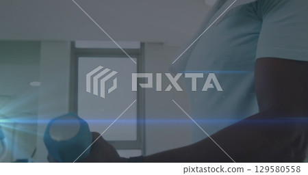 Image of blue light trails against african american fit man working out with dumbbells at home 129580558