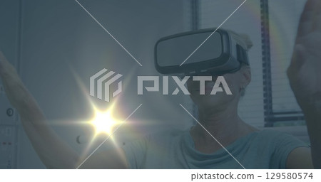 Image of light spots over caucasian businesswoman using vr headset in office 129580574