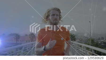 Jogging jogger wearing orange sport shirt and fitness watch on white metal bridge with earphones 129580629