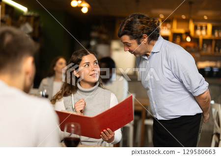 Man waiter writes down girls order. Employee serve couple clients in cafe Man waiter writes down girls order. Employee serve couple clients in cafe 129580663