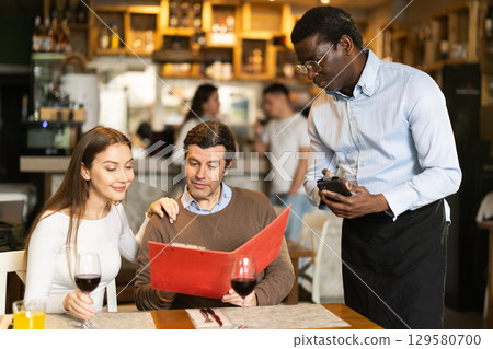 African waiter tells restaurant customers about the range of dishes and wines 129580700
